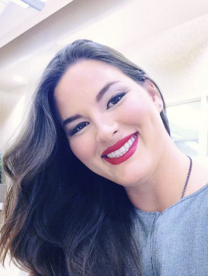 A young Caucasian woman smiling with red lipstick and brown hair wearing a grey dress.